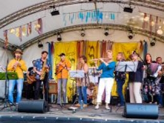 Foto: Orchester mit diversen akustischen Instrumenten spielen auf einer B&uuml;hne