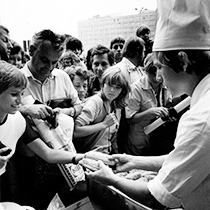 Foto Schwarz-weiß: Junge verteilt Essen an eine ihn umringende Menschenmenge