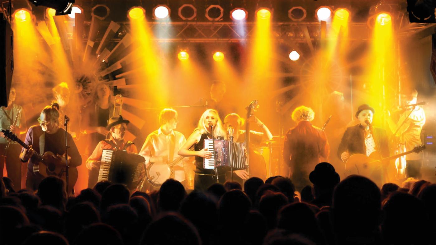 Foto: Musiker auf eine gelb ausgeleuchteten Bühne mit Publikum im Vordergrund