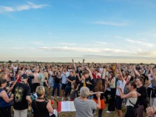 Foto: Sehr viel Publikum auf einer Wiese. Musikgruppe spielt im Vordergrund.