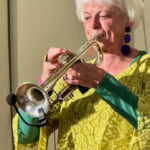 Foto: Frau in gelbem Gewand spielt Trompete