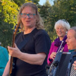 Foto: Mann an der Bassgitarre, im Hintergrund Frau am Akkordeon und Frau an der Trompete - alle lachen